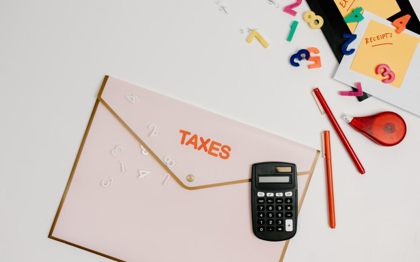 A folder with the word "TAXES" on it. There is various stationery scattered around the folder.